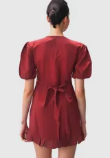 Vestido corto negro con escote en V, mangas cortas abullonadas, corte cruzado con volantes y lazo lateral.