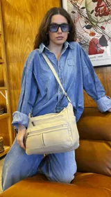 Bandolera de símil cuero color beige, con tres bolsillos frontales con cierre, un bolsillo trasero con cierre y bolsillos internos. Cuenta con una correa larga regulable.