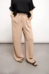 Pantalón color beige de tiro alto, corte suelto y elástico ajustable en la cintura. Confeccionado en poliéster con textura arrugada.