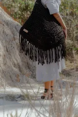 Bolso grande tejido a crochet con trapillo color marrón, con flecos en la parte inferior y etiqueta de cuero con el logo de la marca.