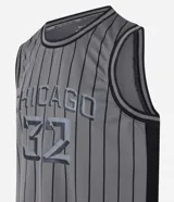 Musculosa deportiva de baloncesto gris con rayas verticales negras, cuello y sisas con ribete negro, y estampado frontal con la palabra "Chicago" y el número "32" en gris.