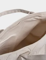 Bolso tipo shopper color beige, con diseño acolchado y pespuntes ondulados. Tiene doble asa de hombro y correa extraíble regulable.