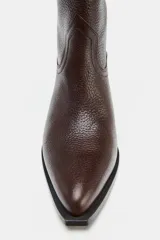 Bota alta de mujer color marrón oscuro, confeccionada en piel de efecto granulado. Presenta un diseño tipo cowboy con doble tirador en la caña para facilitar el calce (pull on) y un tacón medio de 5 cm. La punta es ligeramente afilada.