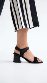 Sandalias de cuero negro con dos tiras, una sobre los dedos y otra al tobillo con cierre de velcro. Tacón bloque bajo.