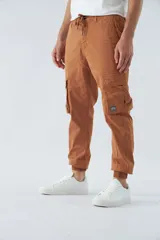 Pantalón cargo color marrón con corte slim, elástico en cintura y cordón ajustable, bolsillos cargo con botones y puños elásticos. Confeccionado en algodón y spandex.