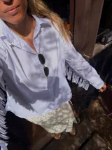 Camisa blanca de mangas largas con flecos en la espalda y en las mangas.