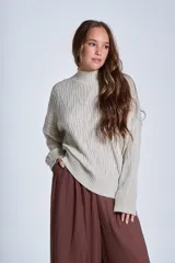 Sweater color crema de punto trenzado, con cuello alto y mangas largas.