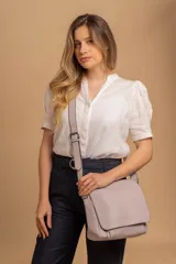 Bandolera de hombro color gris claro, con solapa frontal y correa ajustable. Presenta un diseño simple y práctico, ideal para uso diario.