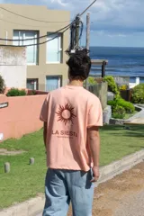 Remera color salmón con estampa en la espalda que incluye un sol y el texto "LA SIESTA TEMPORADA 2024".
