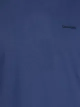 Remera azul de manga corta con cuello redondo y logo de Calvin Klein bordado en el pecho. Presenta una cinta distintiva en los hombros.