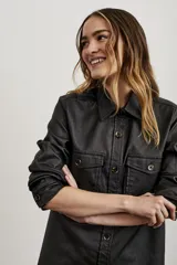 Sobrecamisa negra de textura simil cuero, con cuello camisero, cierre frontal con botones, mangas largas con puños abotonados, dos bolsillos con solapa en el pecho y corte recto.