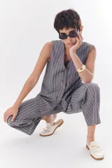 Chaleco gris con finas rayas verticales blancas, con cuello en V, cierre frontal con botones y bolsillos laterales.