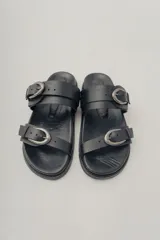 Sandalia plana de cuero color caramelo, estilo 'slide' o 'dos tiras', con hebillas ajustables de metal dorado en cada tira.