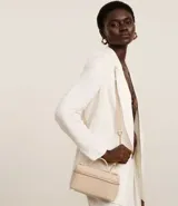 Cartera femenina tipo baú pequeña color beige, con textura tressê, correa de mano fija, cierre por cremallera y asa larga desmontable.