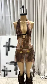 Vestido corto de tela transparente con estampado tipo mármol o tie-dye en tonos marrones, grises y óxido. Diseño halter con escote pronunciado en V y tirante fino negro en el centro del busto. Presenta detalles drapeados o con volados asimétricos en la falda.