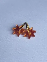 Aros colgantes con forma de estrella color naranja, hechos de acrílico y con aros dorados.