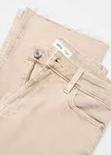 Pantalón de jean color beige, de corte flare, tiro alto y largo crop con terminación desflecada.