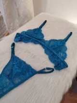 Conjunto de lencería de dos piezas (corpiño y bombacha tipo colaless/tanga) de encaje floral, color verde petróleo/turquesa oscuro. El corpiño es triangular con tirantes ajustables y la bombacha es de corte bajo con bordes festoneados.