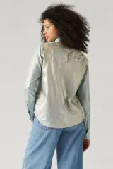 Camisa de manga larga con botones, confeccionada en tela brillante color celeste con efecto óptico. Tiene cuello clásico, dos bolsillos con solapa abotonada en el pecho y corte recto.