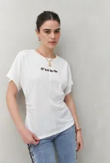 Remera blanca de manga corta con bordado frontal "C’est la vie", calce relajado y frunces laterales.