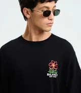 Remera de algodón negra, corte oversized, con estampa frontal de una flor estilizada en tonos rojo, amarillo y verde, y el texto "Balance ESTD. 1995" en blanco.