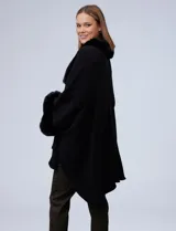 Ruana o poncho negro de tejido suave, con cuello y puños adornados con apliques de piel sintética (faux fur).