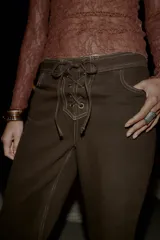 Jeans de tiro alto color marrón oscuro, con pernera recta y detalle de cordones cruzados en la parte delantera central. Presenta costuras contrastantes en color claro.