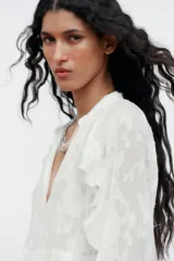 Camisa blanca de cuello redondo con escote en V y mangas largas acampanadas con volantes.