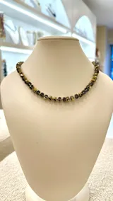 Collar corto de cuentas facetadas en tonos dorados y grises.