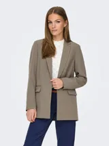 Blazer largo color marrón topo, de corte holgado y tejido sastrero con trama twill. Tiene cuello con solapa y bolsillos delanteros funcionales.