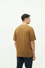Remera color marrón con cuello redondo y manga corta. Presenta un bordado en el lado izquierdo del pecho con un diseño abstracto y texto.