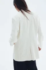 Blazer entallado color blanco con finas rayas verticales negras, solapas de pico, cierre de un botón, bolsillos delanteros de parche y puños con abertura y botón. Forrado.