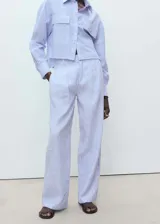 Pantalón de lino a rayas verticales azules y blancas, de corte wide leg, tiro medio, con trabillas, cierre de cremallera y botón, y dos bolsillos laterales.