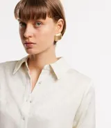 Camisa color crema en crepé con cuello solapa, abotonado frontal, mangas largas y textura de flores tramadas en el tejido.
