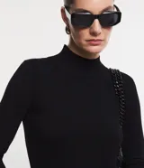 Suéter de punto color crema, con cuello alto, mangas largas con botones en los puños y bajo asimétrico.