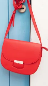 Bandolera roja de símil cuero con correa extensible y cierre con tapa y presilla.