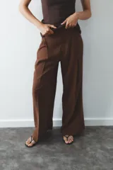 Pantalón color ladrillo de tiro medio con trabillas, detalle de pliegues, bolsillos laterales y falsos bolsillos de vivo en la espalda. Cierre frontal con cremallera y botón.