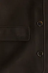 Campera corta de color marrón oscuro con cuello camisero, cierre frontal mediante botones y dos bolsillos delanteros con solapa. Presenta un diseño forrado y corte recto.