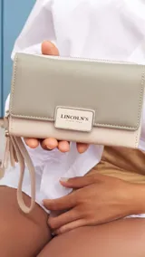 Billetera mediana marca Lincoln's confeccionada en cuero sintético con diseño bicolor. Presenta una tapa en tono dorado metalizado con cierre de presilla y cuerpo negro con compartimento de cremallera. Cuenta con múltiples divisiones internas para tarjetas, billetes y monedas, además de una práctica correa de mano.