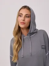 Canguro gris con capucha corta, bolsillo tipo canguro y parche con logo de la marca Rusty en el pecho. Tiene efecto lavado y costuras a la vista.