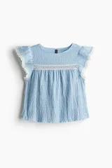 Blusa celeste con textura arrugada, cuello redondo, mangas cortas con volados y detalles de encaje blanco en el canesú y los bordes de las mangas.