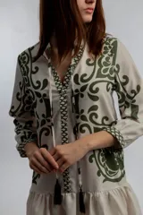 Vestido corto color crema con estampado de motivos geométricos en verde. Tiene cuello mao con lazo y borlas, mangas 3/4 y falda con volantes.