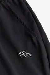 Pantalón deportivo negro de corte ajustado (slim fit) con cintura elástica y cordón de ajuste oculto. Presenta bolsillos al bies y un pequeño logo blanco en la pierna derecha. Confeccionado en tejido funcional DryMove™ con stretch en cuatro direcciones.