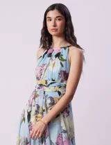 Vestido largo de gasa estampada con flores en tonos celeste, rosa y verde. Tiene cuello halter con abertura en forma de ojal, corte en la cintura con faja plisada y abertura central en la espalda con cierre invisible.