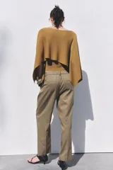 Pantalón color verde oliva de tiro medio con cintura con trabillas, bolsillos laterales, pinzas delanteras y raya planchada. Cierre frontal con cremallera, botón y ganchos metálicos.