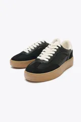 Zapatillas deportivas negras con detalles en cuero sintético y suela de goma color caramelo.