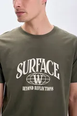 Remera verde militar de manga corta con estampa frontal blanca con la palabra 'Surface' y la frase 'Beyond Reflections'.