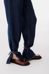 Pantalón de jean azul oscuro de corte recto, tiro alto, con cintura con detalle de lazo y terminaciones desflecadas en la cintura y los tobillos.