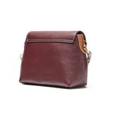 Bandolera pequeña de material sintético color bordó, con textura granulada. Presenta una solapa frontal con costuras decorativas blancas y un logo metálico con las letras "XL". Incluye una correa ancha de tela con diseño a rayas blancas y marrones, ajustable y desmontable, y herrajes metálicos dorados.