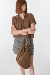 Bolso tipo hobo de cuero color visón con cierre superior y correa de hombro.